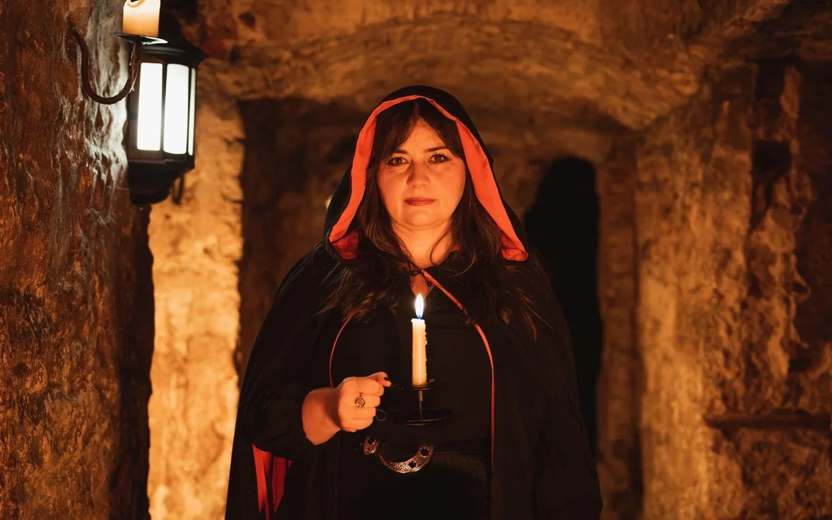 A guide holding a candle in a low stone chamber under the South Bridge