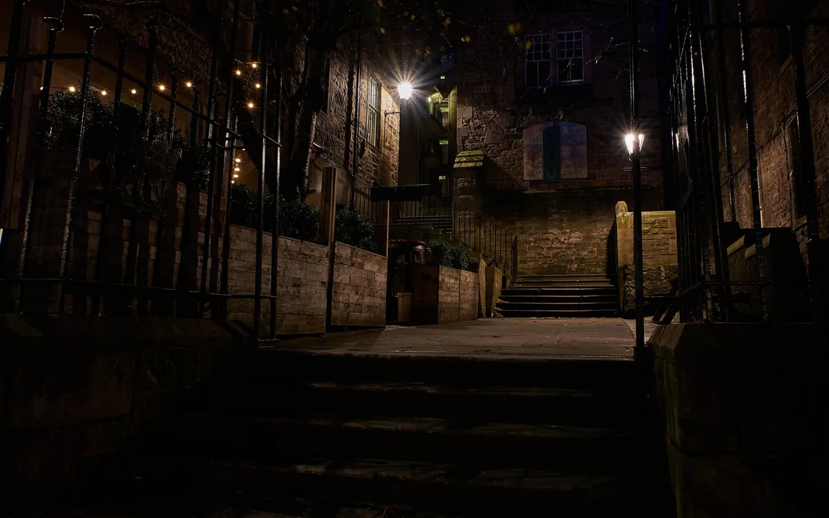 A narrow Edinburgh close at night with lamplight on wet cobbles